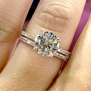 Close-up of a six-prong round cut moissanite ring with micro-pave band on a finger