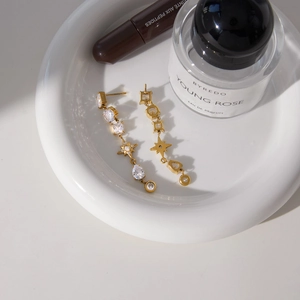 Macro view of gold zircon star fringe earrings displayed on a white ceramic dish