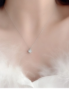 Close-up of S925 silver moissanite pendant necklace worn by a model on a white feather dress