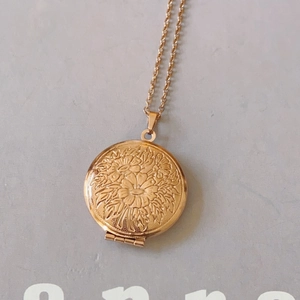 Macro detail of golden round locket necklace featuring embossed floral pattern and hinge