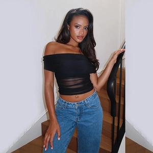 Detail of sheer black off-shoulder mesh top with ruffles and high-waist denim jeans