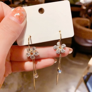 Détail de boucles d'oreilles fleurs à cinq pétales avec zircons et chaîne dorée