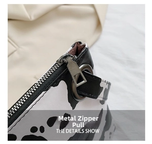 Detailed macro view of the sleek metal zipper hardware on a black and white cow print handbag