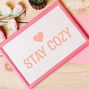Pink decorative art frame with Stay Cozy lettering and heart icon on wood background