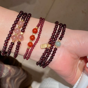 Close-up of stacked garnet beaded bracelets with Fu charm and strawberry quartz beads