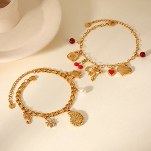 Detailed view of gold Figaro bracelets with heart, cherry and shell charms and pearls
