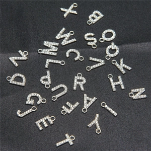 Close-up of silver alphabet pendants with rhinestones on black fabric background