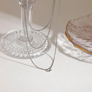 Close-up of triple-layered silver snake chains and beaded necklace with cubic zirconia pendant