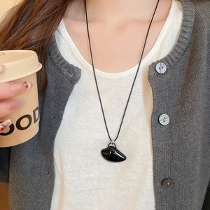 Close-up of minimalist black irregular pendant necklace worn on white t-shirt and grey cardigan