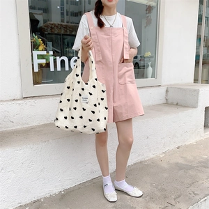 Street style view of a beige canvas tote bag with black heart flocking and logo tag