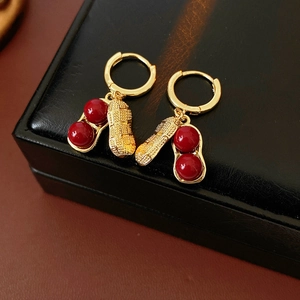 Detail of gold peanut-shaped earrings with red beads on a black jewelry box