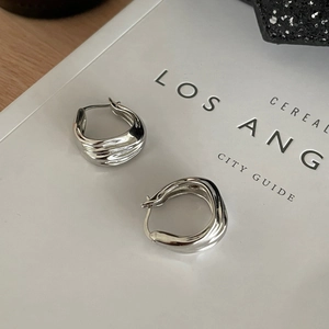 Detailed view of silver hoop earrings with irregular flowing ripple texture and metallic finish
