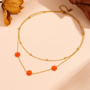 Detail of double-layer stainless steel necklace with orange daisy flower pendants