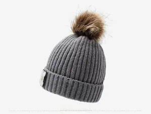 Detail view of the gray ribbed knit beanie with brown faux fur pom and side patch