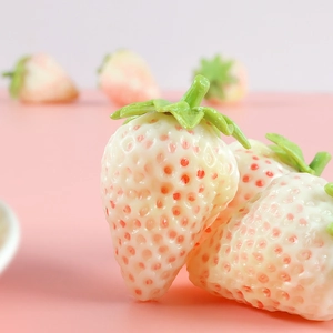 Macro shot of realistic white PVC strawberry model with green leaves on pink background
