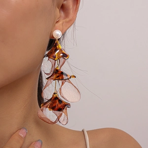 Detailed view of layered amber acrylic petals and white pearl drop earrings on model