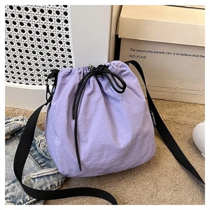 Detail of purple drawstring bucket bag featuring wrinkled texture and black wide strap