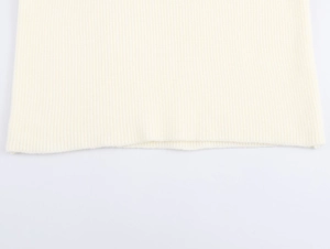 Nahaufnahme des gerippten Stricksaums an einem cremefarbenen, modischen Strickkleid