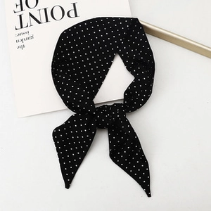 Close-up of black and white polka dot bow headband on a minimal white surface