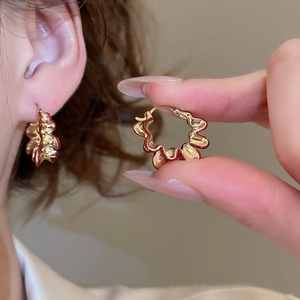 Close-up of gold wave-shaped earrings with red enamel edges worn by a model