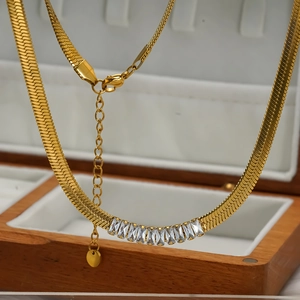 Golden snake chain necklace with rectangular white zircons on a wooden jewelry box