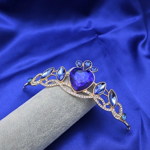 Close-up of golden alloy crown with heart-shaped blue sapphire crystal on blue silk