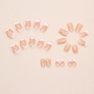Close-up of nude pink press-on nails with irregular white tips and gold foil accents