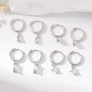 Silver hoop earrings set with square, drop, and rectangle zircon charms in a flat lay view
