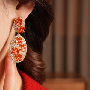Close-up of vintage gold oval earrings with zircon micro-pave and red floral crystal pattern