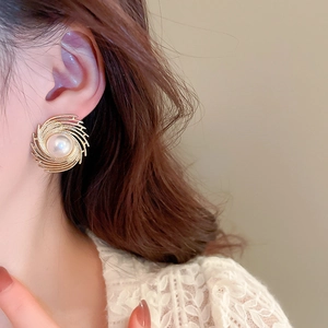 Macro detail of golden spiral swirl earrings with white pearl center on model
