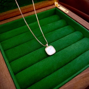 Detail of square shell pendant on gold necklace inside a green velvet jewelry box