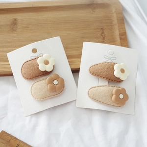 Detailed view of floral felt snap hair clips in milk tea colors on white fabric