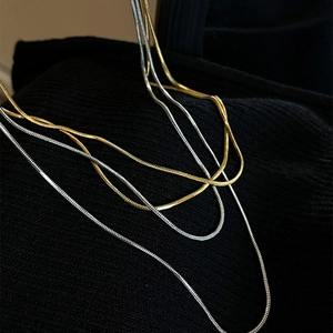 Detail of sleek gold and silver snake chains on dark knitwear for a layered luxury look