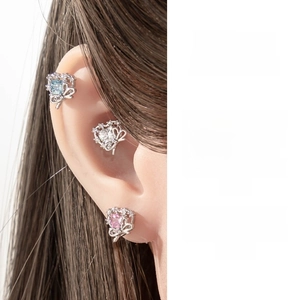 Macro detail of silver cartilage earrings with blue zircon bow and heart-shaped crystals