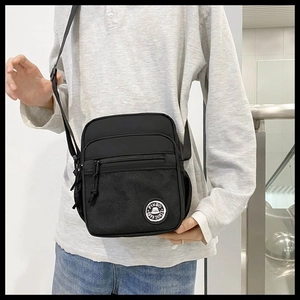 On-body shot of a black minimalist messenger bag with adjustable strap and mesh pocket