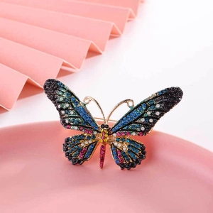 Elegant gold butterfly brooch with colorful rhinestones on a decorative pink tray