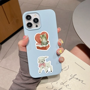 Hand holding a blue iPhone case featuring vintage cat and lamb coquette stickers
