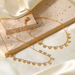 Elegant gold stainless steel necklace with sparkling white rhinestone tassels on silk background