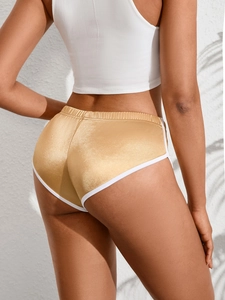 Dettaglio di pantaloncini sportivi oro lucido con bordo a contrasto bianco e vestibilità slim