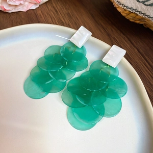 Detailed close-up of long green shell earrings with translucent layered round discs