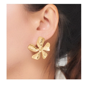 Close-up of golden five-petal flower earrings with textured petals on a female model