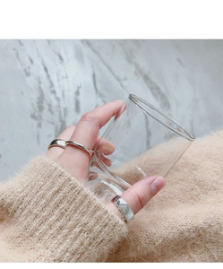 Minimalist silver rings worn on fingers holding a glass with a marble background