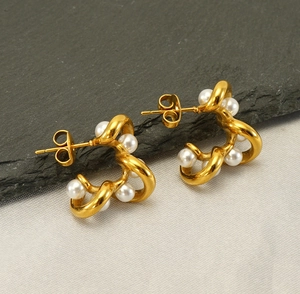 Detail of twisted gold earrings with small pearls on a dark textured stone background