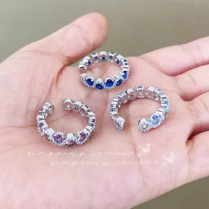 Close-up of three silver ear cuffs set with blue and purple gemstones on a hand