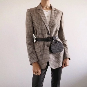 Detailansicht eines braunen Blazers mit Hahnentrittmuster und schwarzer Gürteltasche