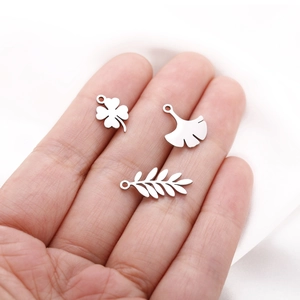 Detailed macro view of clover, ginkgo, and olive branch stainless steel charms held in hand