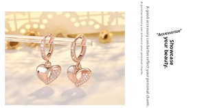 Macro shot of rose gold heart earrings with white crystals on a transparent stand