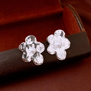 Macro shot of silver flower earrings with textured liquid metal petals and center pearl