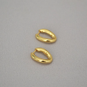 Primer plano de pendientes minimalistas de latón dorado en forma de U sobre gris