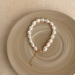 Detailed view of white baroque pearl bracelet with adjustable gold clasp on beige plate
